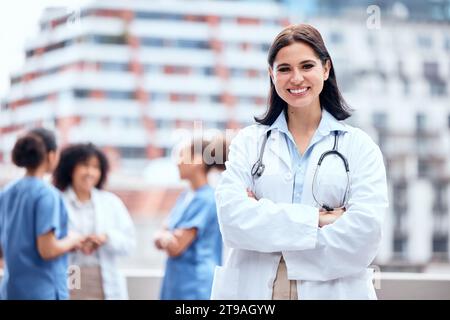 Femme, médecin et portrait heureux en plein air avec les bras croisés à l'hôpital, clinique ou collègues sur le toit pour une pause., chirurgien, sourire et confiance sur Banque D'Images