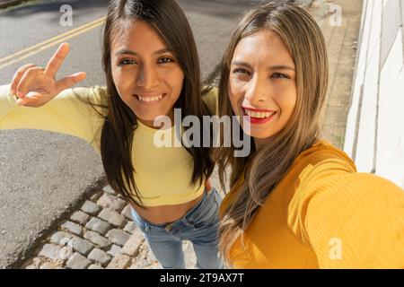 Deux belles jeunes femmes riant en prenant un selfie avec leur téléphone portable. Technologie, communications, concept d'amitié. Banque D'Images