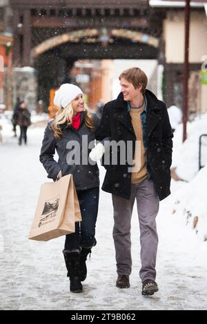 Jeune couple attrayant shopping dans un village avec la neige tombant. Banque D'Images