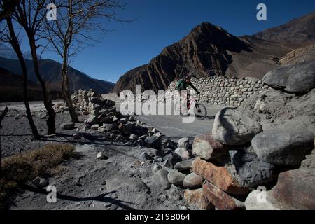 Un homme monte un vélo de montagne par mur de roche sur un chemin de terre avec des montagnes à proximité. Banque D'Images