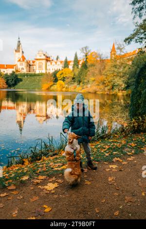 Un garçon avec un chien corgi près du lac dans le château de Pruhonice Banque D'Images