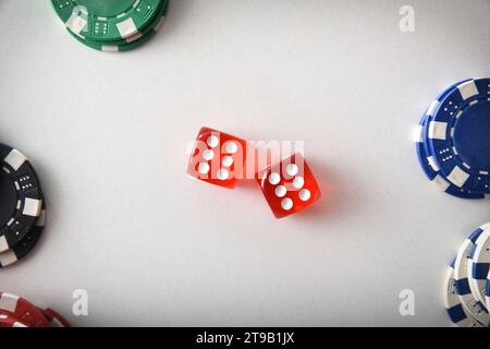 Fond de jeu de dés de casino avec deux dés rouges au centre et pile de jetons de Paris de couleur différente aux extrémités isolées sur la table blanche. Vue de dessus Banque D'Images