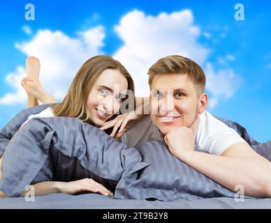 Heureux beau couple dans le lit isolé sur fond de ciel bleu, concept de séjour à la maison, fond de quarantaine coronavirus, auto-isolement, style de vie à Banque D'Images