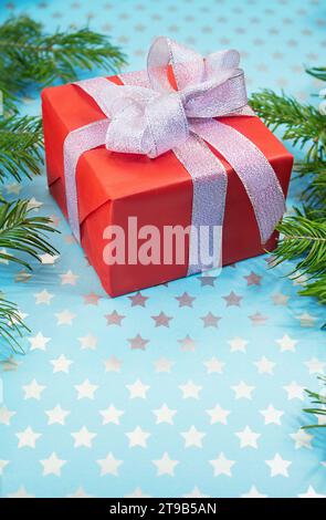Boîte cadeau rouge avec noeud argenté brillant sur fond bleu avec des étoiles et des branches de sapin. Noël, nouvel an, Saint Valentin, anniversaire, vacances. Vertical. Banque D'Images