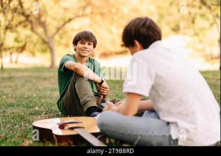 Deux frères passent du temps dans le parc tout en parlant et en jouant de la guitare et assis sur la guitare. Banque D'Images