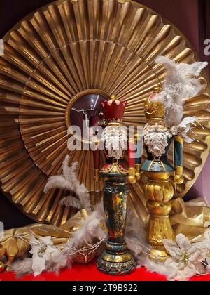 Deux casse-noisettes de Noël sur une table entourée de plumes et arrangement doré de Noël de fleurs, feuilles, lumières et boules de noël. Banque D'Images