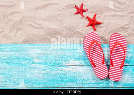 Étoile de mer rouge et tongs sur le sable et planche de bois vue de dessus Banque D'Images
