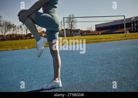 vue courte de sportswoman flexible s'exerçant dans des vêtements d'activité serrés à l'extérieur, étirant la jambe Banque D'Images