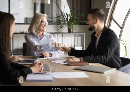 Positive femme d'affaires âgée réussie serrant la main au meilleur travailleur plus jeune Banque D'Images