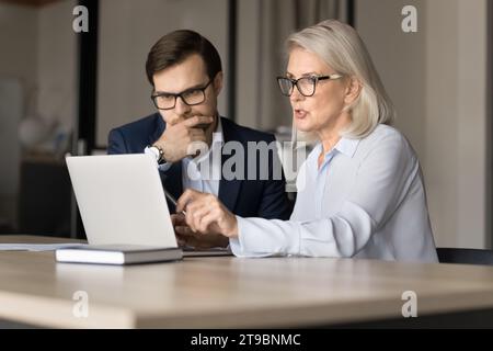 Collègues professionnels sérieux, plus jeunes et plus âgés, dans des lunettes, travaillant ensemble Banque D'Images