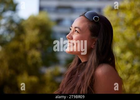 Jeune femme souriante assise dehors et regardant loin Banque D'Images