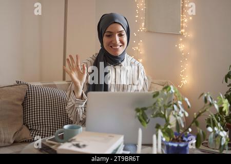 Heureuse femme freelance agitant sur appel vidéo sur ordinateur portable tout en travaillant dans le salon à la maison Banque D'Images