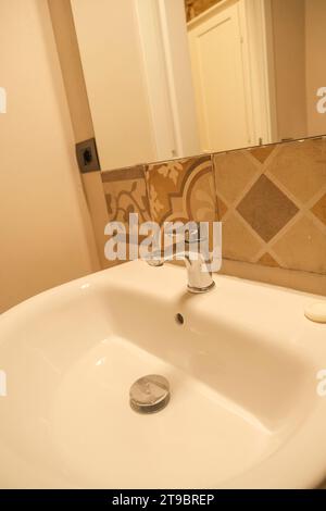 lavabo dans la salle de bains de l'hôtel avec robinet à travers des carreaux artistiques bruns et meubles suspendus blancs. Intérieur de salle de bains Banque D'Images