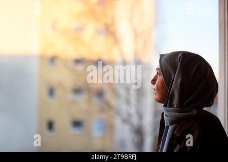 Femme réfléchie en foulard regardant par la fenêtre Banque D'Images