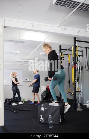 Vue latérale pleine longueur de la jeune femme avec haltère s'exerçant sur le bloc dans la salle de gym Banque D'Images