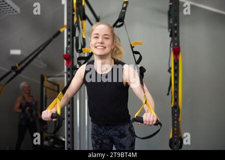 Portrait de jeune femme heureuse appuyée sur des anneaux de gymnastique au club de santé Banque D'Images