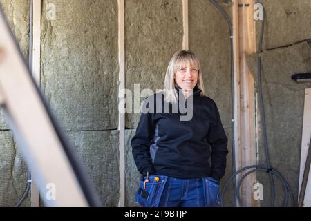 Femme souriante cols bleus avec les mains dans les poches debout contre le mur Banque D'Images