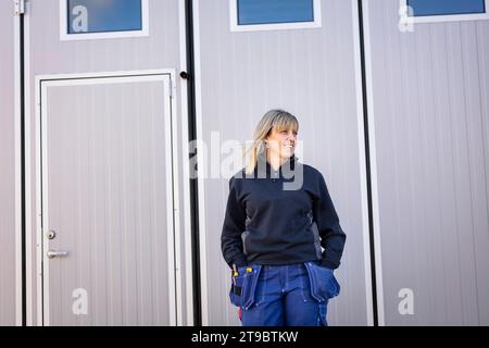 Cols bleus féminins avec les mains dans les poches debout contre la porte Banque D'Images