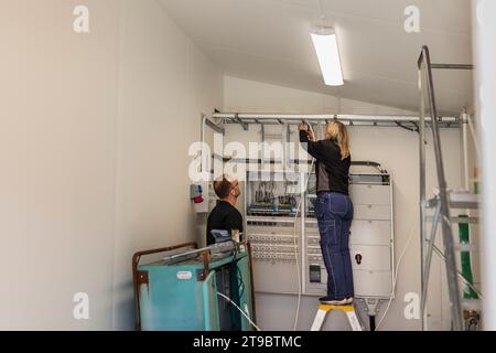 Électricien féminin installant des câbles debout à côté d'un collègue masculin dans la salle des compteurs Banque D'Images
