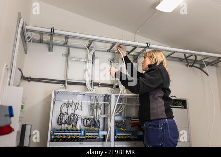 Électricien femelle fixant les fils de câble sur l'échelle dans la salle de compteur à l'industrie Banque D'Images