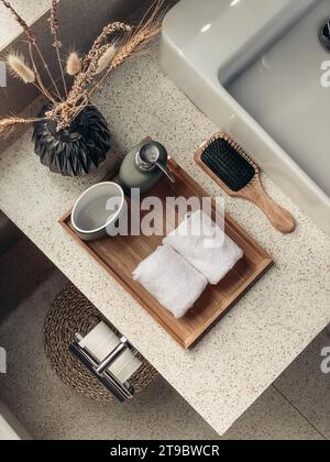 Deux essuie-mains dans la salle de bains avec distributeur de savon liquide sur plateau en bambou et brosse à cheveux, vue du dessus Banque D'Images