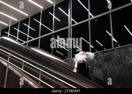 Belgrade, Serbie- 20 novembre 2023 : personne montant l'escalier mécanique du métro, avec les lumières intérieures réfléchissantes et le panneau de l'hôtel Moscou en caractères cyrilliques Banque D'Images