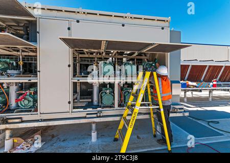 Un travailleur de la construction travaille à l'intérieur d'un carter de compresseur avec des portes ouvertes sur le toit d'un entrepôt de stockage de CO2 froid (réfrigération industrielle) Banque D'Images