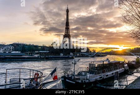 Tour Eiffel au coucher du soleil au bord de la Seine, bateaux de tourisme au drapeau français. Magie parisienne dans une étreinte crépusculaire. Beau panorama de Paris. Banque D'Images