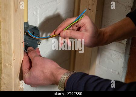 Construire et installer le câblage électrique avec la phase brune, le neutre bleu et le fil de terre jaune dans une maison en utilisant des boîtiers muraux creux Banque D'Images