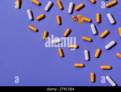 Pilules de vitamines orange et blanches sur fond violet Banque D'Images