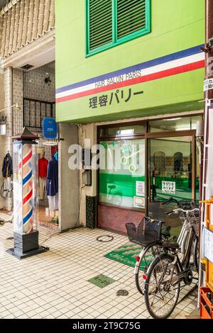 Extérieur du centre-ville d'un coiffeur japonais, «salon de coiffure Paris» avec deux vélos à l'extérieur et barbiers typiques poteau sur le trottoir. Banque D'Images