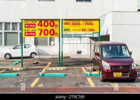 Parking japonais avec de grands panneaux indiquant le prix et les horaires, 400 yens ou 700 yens selon l'heure de la journée. Jour, soleil éclatant. Deux voitures garées Banque D'Images