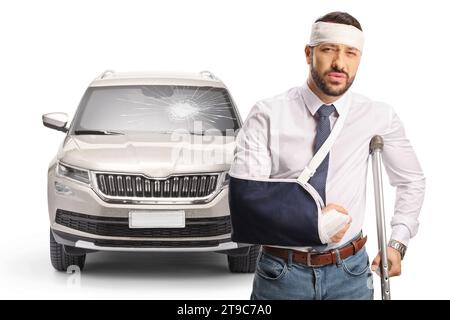 Conducteur blessé après un accident de voiture debout avec une béquille devant un véhicule avec pare-brise cassé isolé sur fond blanc Banque D'Images