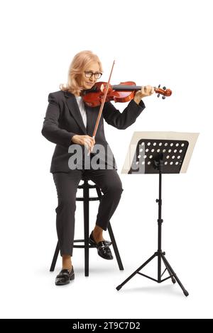 Plan complet d'une femme mûre sur une chaise jouant du violon et lisant un pupitre de musique isolé sur fond blanc Banque D'Images