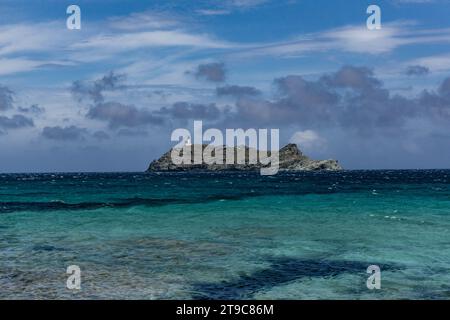 Une petite île rocheuse dans la mer Méditerranée avec un phare blanc, entourée d'eaux turquoises contre un ciel nuageux bleu. Corse, France. Banque D'Images