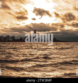 Alors que le soleil brille adieu, sa lueur illumine la sentinelle du rivage - un phare se dresse au milieu de la mer embrassant au crépuscule. Golden Hour. Banque D'Images