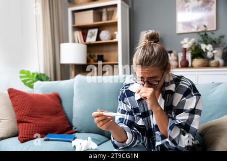 Femme triste célibataire se plaignant tenant un test de grossesse assis sur un canapé dans le salon à la maison, femme stressée, positive ou négative te médicale Banque D'Images