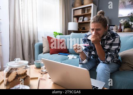 Femme triste célibataire se plaignant tenant un test de grossesse assis sur un canapé dans le salon à la maison, femme stressée, positive ou négative te médicale Banque D'Images