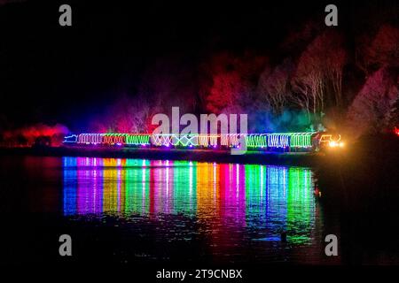 Kingswear, Devon, Royaume-Uni. 24 novembre 2023. Le train des lumières de Noël sur le chemin de fer à vapeur de Dartmouth dans le Devon, qui circule entre le 24 novembre et le 30 décembre 2023, se reflète dans les eaux calmes de la rivière Dart alors qu'il se dirige vers Kingswear dans le Devon sur son voyage de Paignton. Les voitures et les locomotives à vapeur du service festif sont éclairées à l'intérieur et à l'extérieur avec des lumières colorées. Crédit photo : Graham Hunt/Alamy Live News Banque D'Images