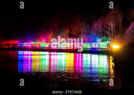 Kingswear, Devon, Royaume-Uni. 24 novembre 2023. Le train des lumières de Noël sur le chemin de fer à vapeur de Dartmouth dans le Devon, qui circule entre le 24 novembre et le 30 décembre 2023, se reflète dans les eaux calmes de la rivière Dart alors qu'il se dirige vers Kingswear dans le Devon sur son voyage de Paignton. Les voitures et les locomotives à vapeur du service festif sont éclairées à l'intérieur et à l'extérieur avec des lumières colorées. Crédit photo : Graham Hunt/Alamy Live News Banque D'Images