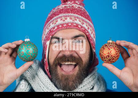 Homme heureux dans l'usure d'hiver avec des jouets d'arbre de Noël de couleur dorée. Décorations et ornements de vacances. Célébration de Noël ou du nouvel an. Homme barbu Banque D'Images