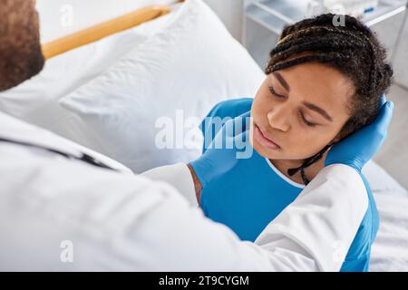 malade jolie femme afro-américaine fermant les yeux pendant que son médecin indien examine ses ganglions lymphatiques Banque D'Images