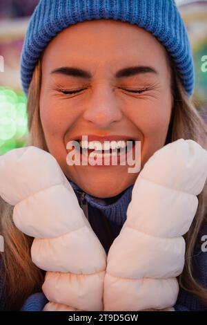 Femme joyeuse et élégante, vêtue de vêtements chauds, s'amuse dans un parc d'attractions hivernal enneigé. Banque D'Images