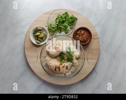 Délicieux poulet à la vapeur au riz (riz au poulet du Hainanais) servir avec de l'ail mariné, du concombre et de la sauce sucrée au Chili sur un plateau rond en bois Aliments halal, Banque D'Images