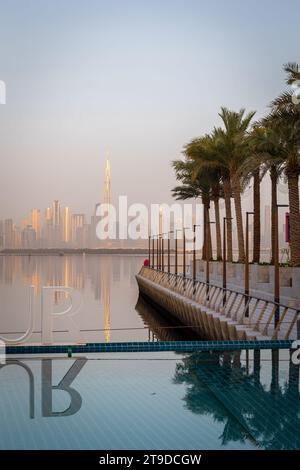 Dubaï, Émirats arabes Unis, 07.02.22. Piscine d'eau turquoise du port de Dubai Creek avec rangée de palmiers et horizon du centre-ville de Dubaï aux couleurs dorées du lever du soleil. Banque D'Images