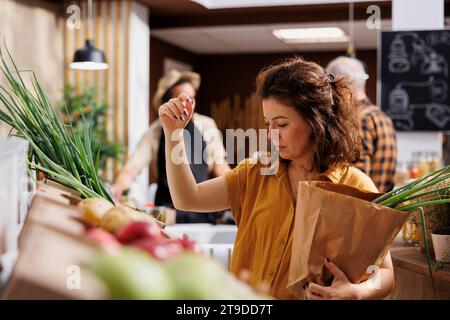 Femme dans le marché des agriculteurs magasinant des légumes sans produits chimiques, cueillant des oignons verts mûrs. Client dans l'épicerie locale gratuite en plastique utilisant le sac en papier décomposable pour éviter le gaspillage excessif Banque D'Images