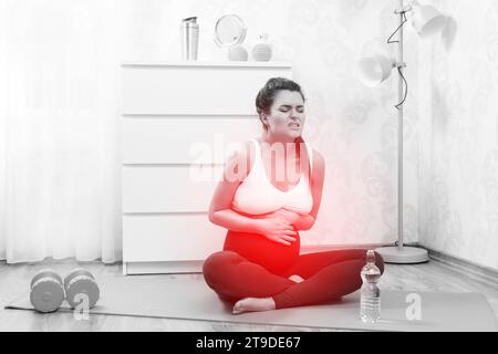 Young pregnant woman feel bad during her fitness workout at home Stock Photo