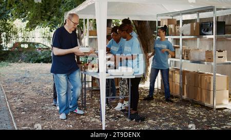 Scène présentant un groupe de bénévoles qui donnent des dons alimentaires à des personnes moins privilégiées. De jeunes bénévoles donnent de leur temps pour aider les nécessiteux et fournir des repas gratuits aux sans-abri. Portable. Banque D'Images