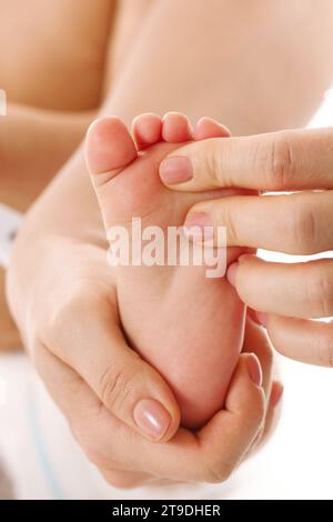 Gros plan d'une mère massant doucement les pieds et les semelles de son petit enfant sur fond blanc. Banque D'Images