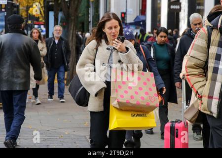 Londres, Royaume-Uni. 24 novembre 2023. Une cliente tient son téléphone portable en marchant dans Oxford Street, dans le centre de Londres. (Image de crédit : © Steve Taylor/SOPA Images via ZUMA Press Wire) USAGE ÉDITORIAL SEULEMENT! Non destiné à UN USAGE commercial ! Banque D'Images